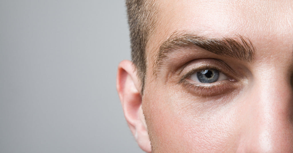 A person with blue eyes and brown hair is standing alone and staring straight ahead. A grey wall is behind them.