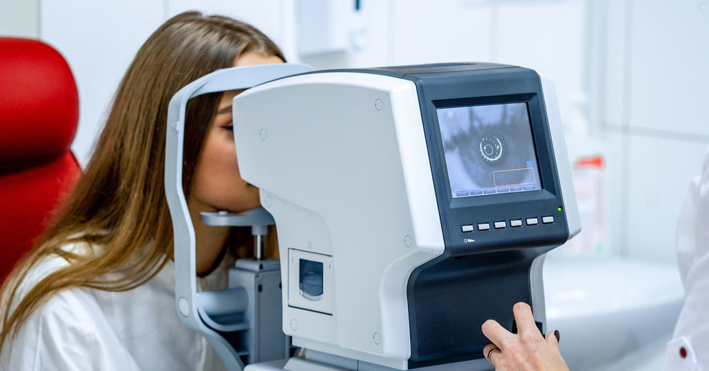 A person in a red chair in an ophthalmologist’s office looking into a machine that displays their eye on a screen.